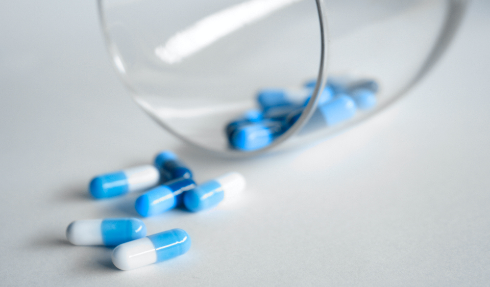 antibiotic capsules, blue and white capped, falling out of glass cup.