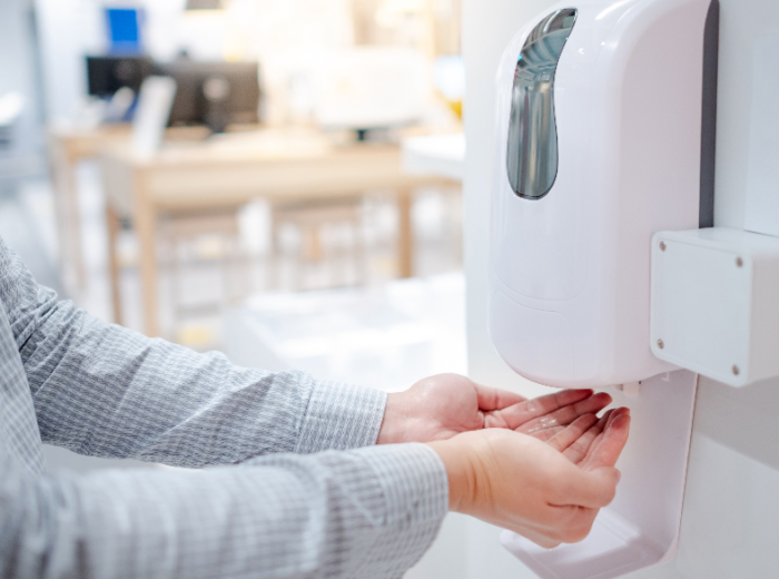 Male hands using automatic hand sanitiser dispensers for hand hygiene in an office.