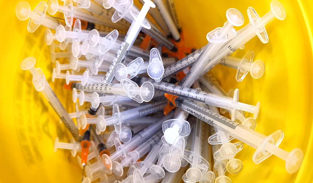 close up of the used vaccine needles in a sharp bin unit