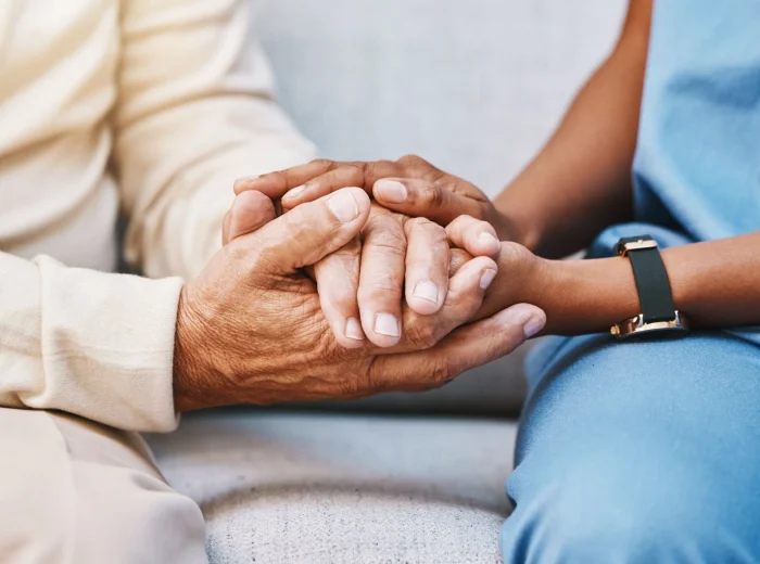 Close-up shot of an elderly person holding hands with a young care home carer.