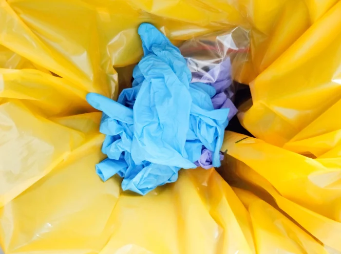 A mix of used blue and purple medical gloves in a yellow waste bag.