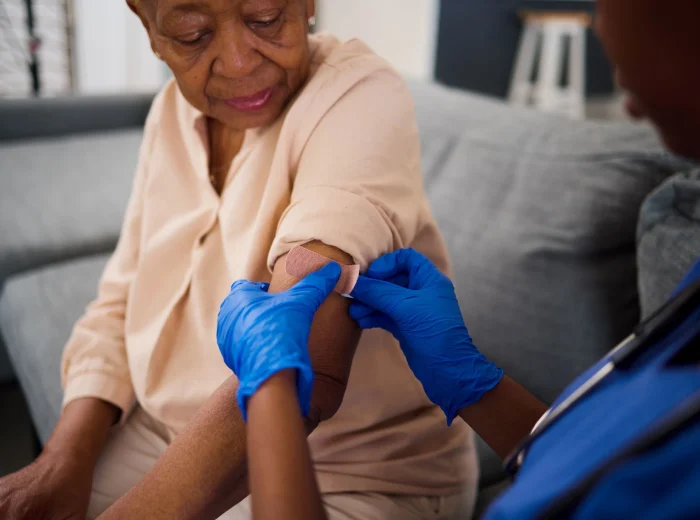 Young nurse placing plaster on elderly woman's arm after receiving injection.