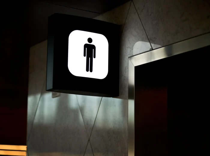 A wall-mounted, illuminated men's toilet sign above a doorframe.
