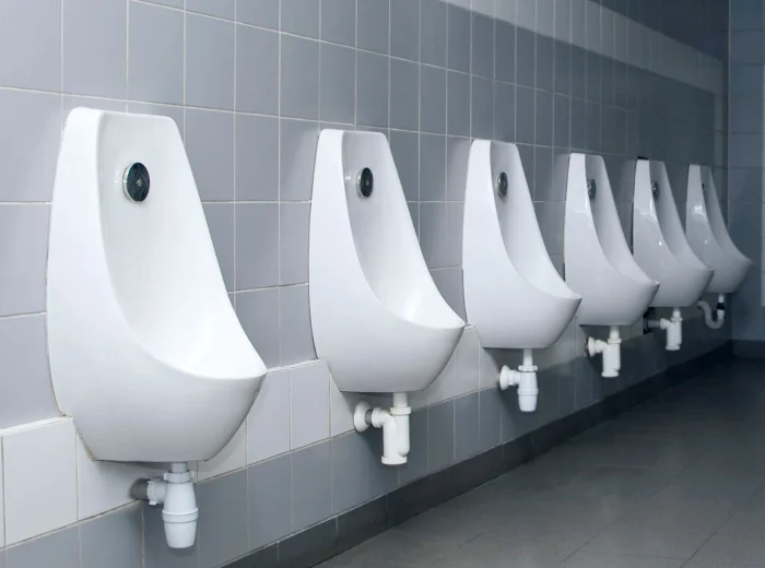 A row of urinals mounted to a white and grey tiled bathroom wall.