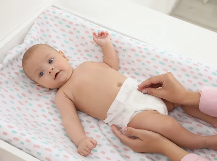 A baby on its back on a baby changing table with a white nappy on.