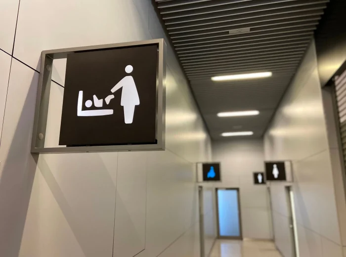 A black square sign attached to a wall with a white icon of a person changing a baby's nappy on a changing table.