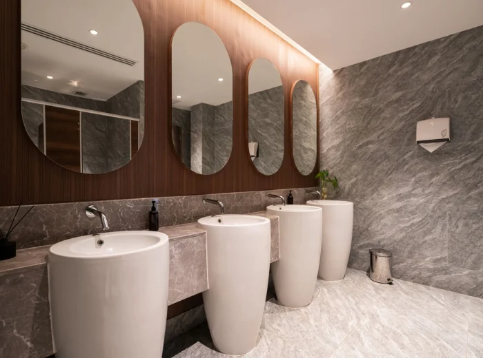 A modern commercial washroom with stone walls and flooring, large round basins, and rounded mirrors fitted to a wooden wall.