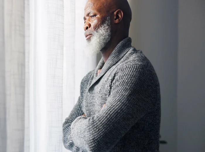 Elderly black man with beard looking pensively out of window.